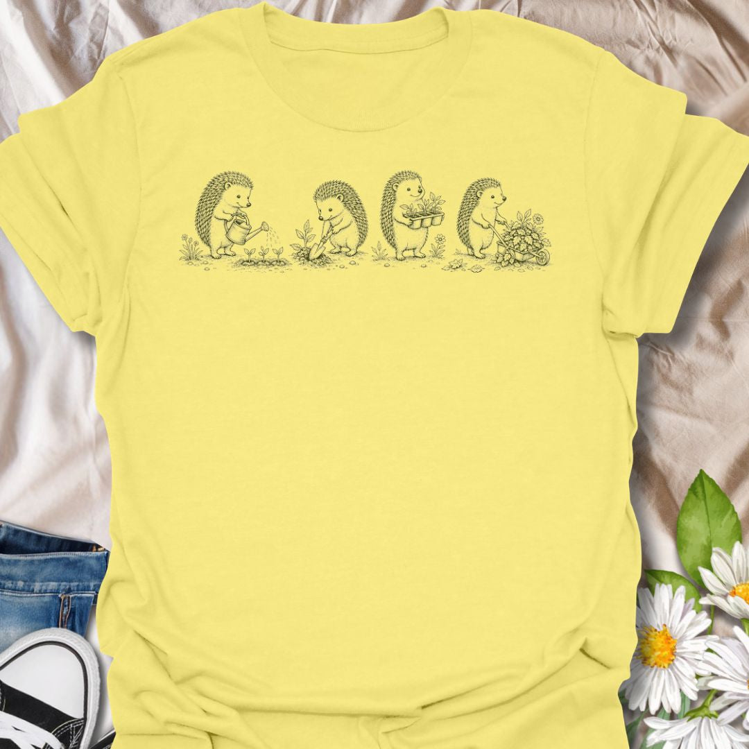 This Gardening Hedgehogs t-shirt is made for gardeners, nature lovers, and woodland animal fans who enjoy sweet vintage-style artwork. Featuring four charming hedgehogs watering, digging, carrying plants, and pushing a flower-filled wheelbarrow, this design has a gentle cottagecore garden feel. Perfect for plant lovers, gardeners, hedgehog fans, wildlife lovers, botanical art fans, and anyone who loves soft nature-inspired designs.