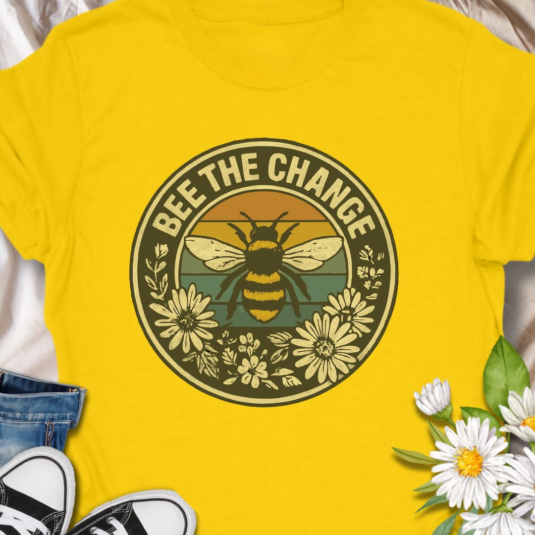 Spread positivity and environmental awareness with this vintage-style “Bee The Change” t-shirt. Featuring a bold bee illustration surrounded by wildflowers and retro sunset colors, it’s perfect for nature lovers, pollinator protectors, and eco-conscious souls. Makes a thoughtful gift for beekeepers, gardeners, or anyone who believes in making a difference—one bee at a time.