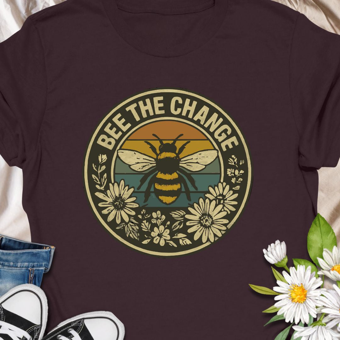 Spread positivity and environmental awareness with this vintage-style “Bee The Change” t-shirt. Featuring a bold bee illustration surrounded by wildflowers and retro sunset colors, it’s perfect for nature lovers, pollinator protectors, and eco-conscious souls. Makes a thoughtful gift for beekeepers, gardeners, or anyone who believes in making a difference—one bee at a time.