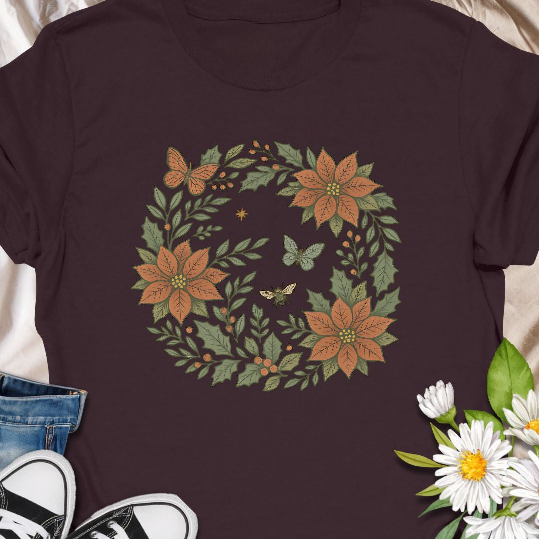 Festive botanical tee featuring a Christmas wreath with poinsettias, bees, and butterflies. Perfect holiday wear for plant lovers.