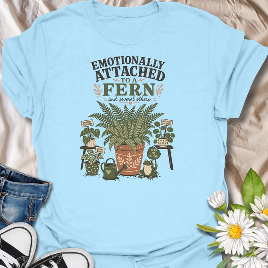 Celebrate your favorite leafy companion with this “Emotionally Attached to a Fern” T-shirt. Featuring a large decorative fern, houseplants, a watering can, and a cheerful frog, it is perfect for devoted plant parents. A charming gift for fern lovers, indoor gardeners, and botanical collectors.