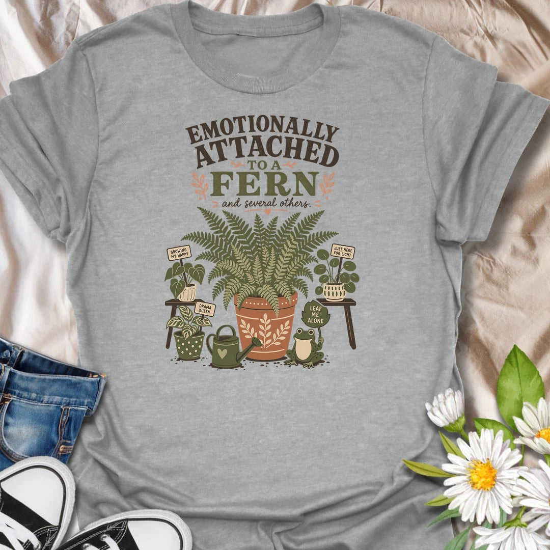 Celebrate your favorite leafy companion with this “Emotionally Attached to a Fern” T-shirt. Featuring a large decorative fern, houseplants, a watering can, and a cheerful frog, it is perfect for devoted plant parents. A charming gift for fern lovers, indoor gardeners, and botanical collectors.
