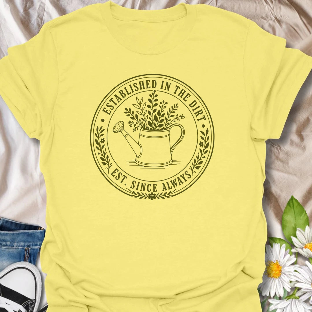 This Established In The Dirt t-shirt is made for gardeners who have always felt happiest with soil on their hands and something green to grow. Featuring a vintage-style circular badge with a watering can, leafy plant details, and the phrase Est. Since Always, this design has a simple botanical look that feels classic, earthy, and easy to wear. Perfect for gardeners, plant lovers, backyard growers, flower fans, vegetable gardeners, and anyone whose happy place is firmly rooted in the dirt.