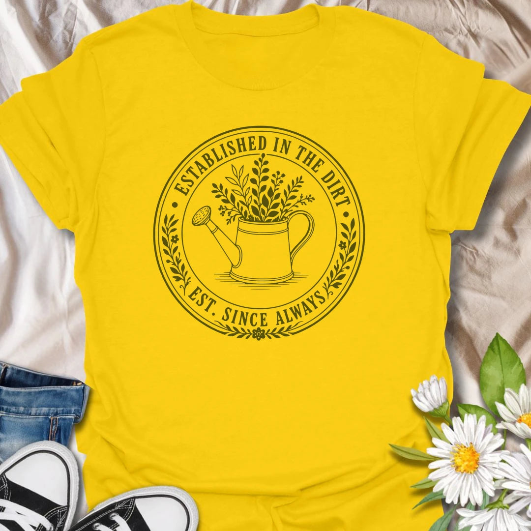 This Established In The Dirt t-shirt is made for gardeners who have always felt happiest with soil on their hands and something green to grow. Featuring a vintage-style circular badge with a watering can, leafy plant details, and the phrase Est. Since Always, this design has a simple botanical look that feels classic, earthy, and easy to wear. Perfect for gardeners, plant lovers, backyard growers, flower fans, vegetable gardeners, and anyone whose happy place is firmly rooted in the dirt.