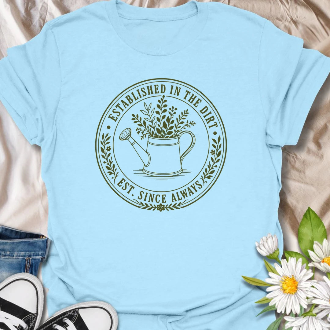 This Established In The Dirt t-shirt is made for gardeners who have always felt happiest with soil on their hands and something green to grow. Featuring a vintage-style circular badge with a watering can, leafy plant details, and the phrase Est. Since Always, this design has a simple botanical look that feels classic, earthy, and easy to wear. Perfect for gardeners, plant lovers, backyard growers, flower fans, vegetable gardeners, and anyone whose happy place is firmly rooted in the dirt.