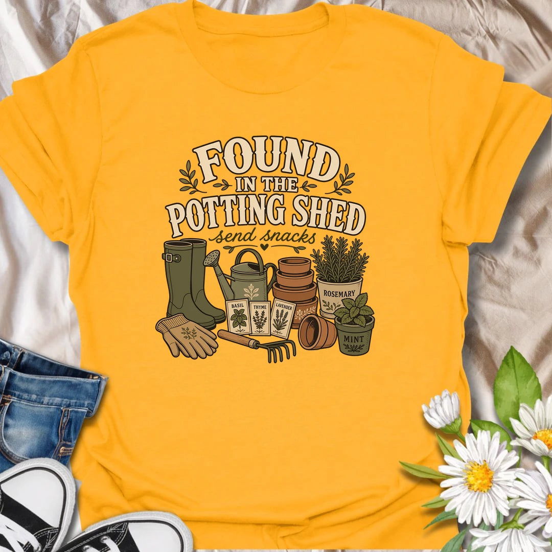 A cozy gardening T-shirt for anyone happiest among pots, herbs, seeds, and soil. The design features gardening boots, a watering can, terracotta pots, seed packets, and fresh herbs. A fun gift for potting shed lovers, herb gardeners, and women who disappear into the garden for hours.