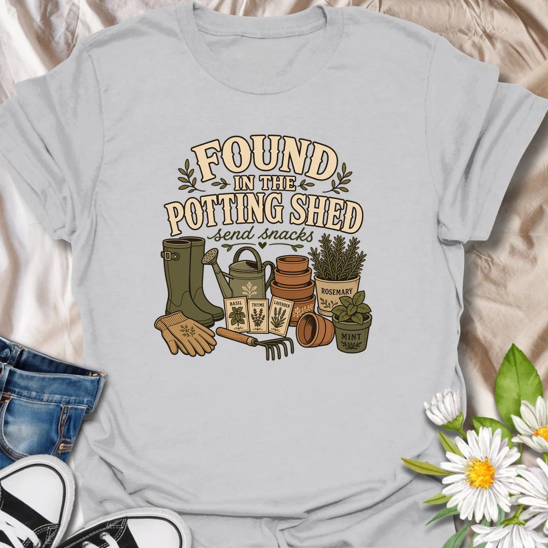 A cozy gardening T-shirt for anyone happiest among pots, herbs, seeds, and soil. The design features gardening boots, a watering can, terracotta pots, seed packets, and fresh herbs. A fun gift for potting shed lovers, herb gardeners, and women who disappear into the garden for hours.