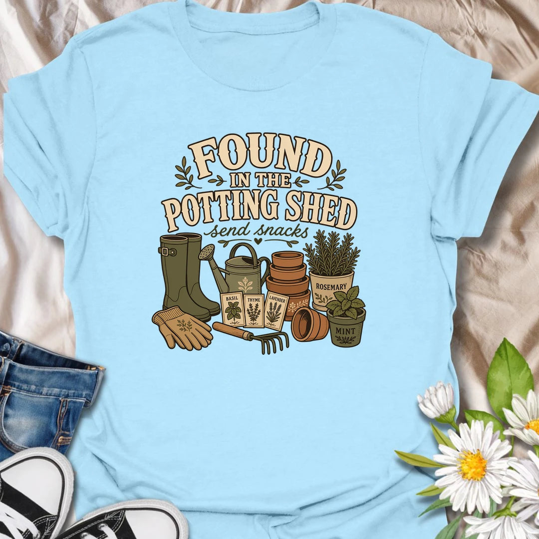 A cozy gardening T-shirt for anyone happiest among pots, herbs, seeds, and soil. The design features gardening boots, a watering can, terracotta pots, seed packets, and fresh herbs. A fun gift for potting shed lovers, herb gardeners, and women who disappear into the garden for hours.