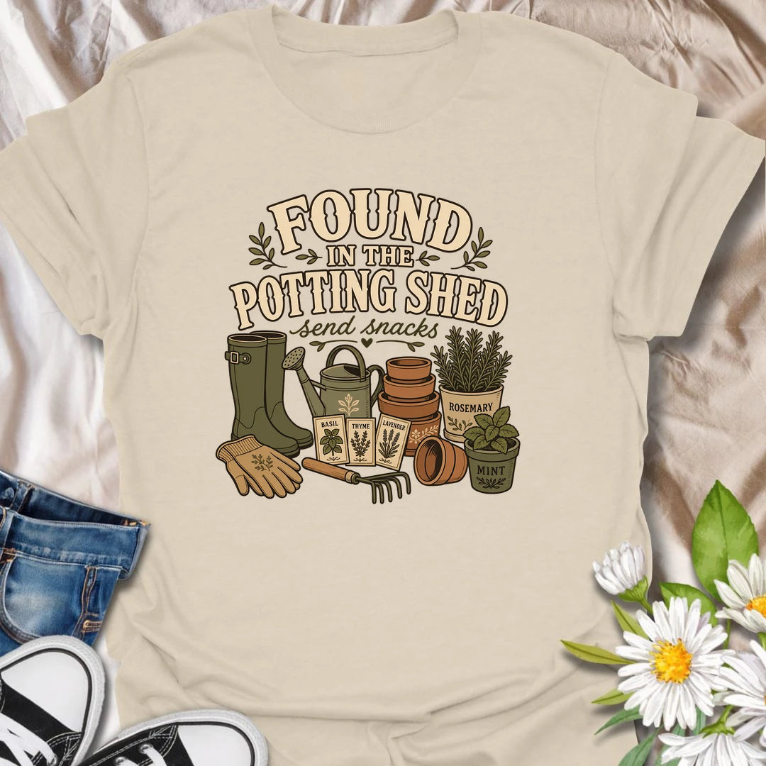 A cozy gardening T-shirt for anyone happiest among pots, herbs, seeds, and soil. The design features gardening boots, a watering can, terracotta pots, seed packets, and fresh herbs. A fun gift for potting shed lovers, herb gardeners, and women who disappear into the garden for hours.