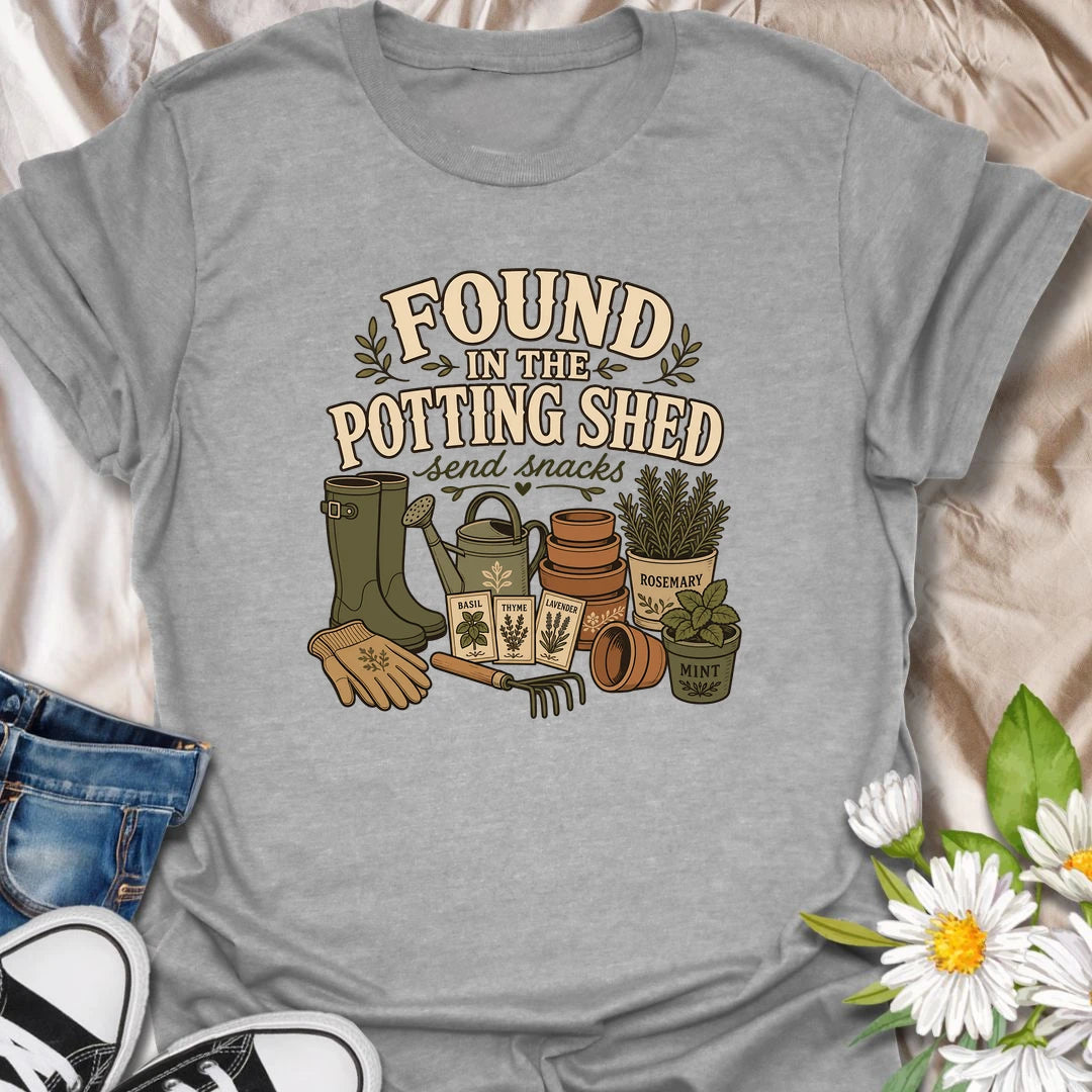 A cozy gardening T-shirt for anyone happiest among pots, herbs, seeds, and soil. The design features gardening boots, a watering can, terracotta pots, seed packets, and fresh herbs. A fun gift for potting shed lovers, herb gardeners, and women who disappear into the garden for hours.