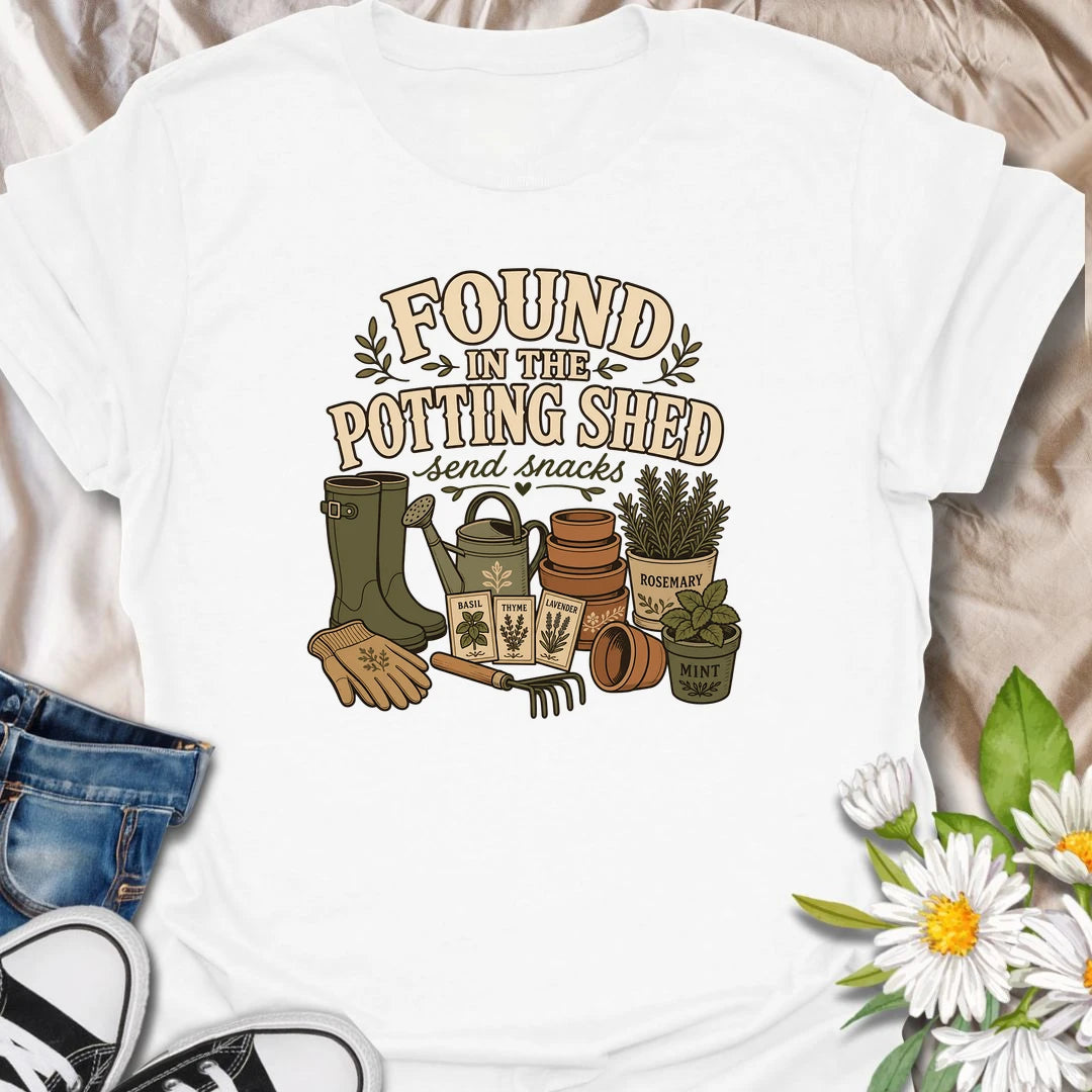 A cozy gardening T-shirt for anyone happiest among pots, herbs, seeds, and soil. The design features gardening boots, a watering can, terracotta pots, seed packets, and fresh herbs. A fun gift for potting shed lovers, herb gardeners, and women who disappear into the garden for hours.