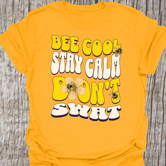 "Bee Cool, Stay Calm, Don't Swat" shaped text in white and yellow with images of bees and flowers.  Gold colored T-shirt