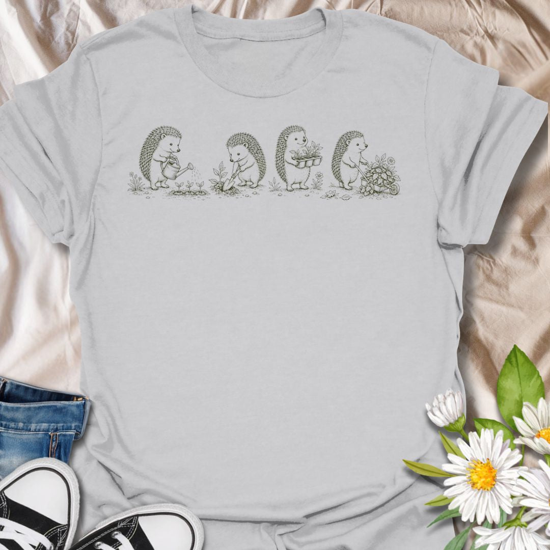 This Gardening Hedgehogs t-shirt is made for gardeners, nature lovers, and woodland animal fans who enjoy sweet vintage-style artwork. Featuring four charming hedgehogs watering, digging, carrying plants, and pushing a flower-filled wheelbarrow, this design has a gentle cottagecore garden feel. Perfect for plant lovers, gardeners, hedgehog fans, wildlife lovers, botanical art fans, and anyone who loves soft nature-inspired designs.