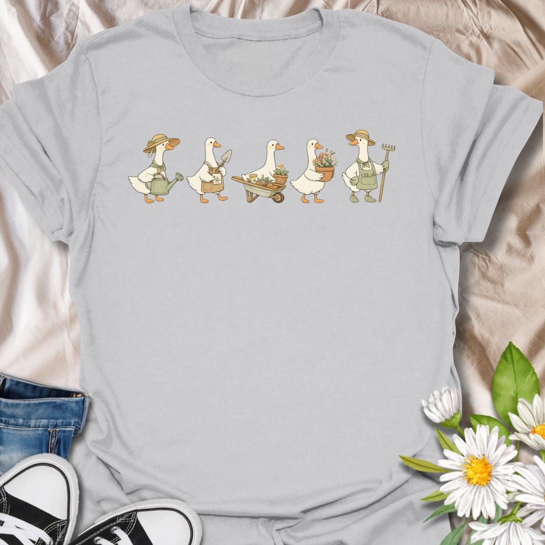 This Gardening Geese t-shirt is made for gardeners, plant lovers, and anyone who enjoys cute nature-inspired artwork with a little humor. Featuring a row of charming geese carrying watering cans, garden tools, flower pots, a wheelbarrow, and fresh plants, this design has a playful cottagecore garden feel that is easy to wear. Perfect for gardeners, duck lovers, plant moms, flower fans, backyard growers, and anyone who thinks garden chores are better with a gaggle of helpful Geese.