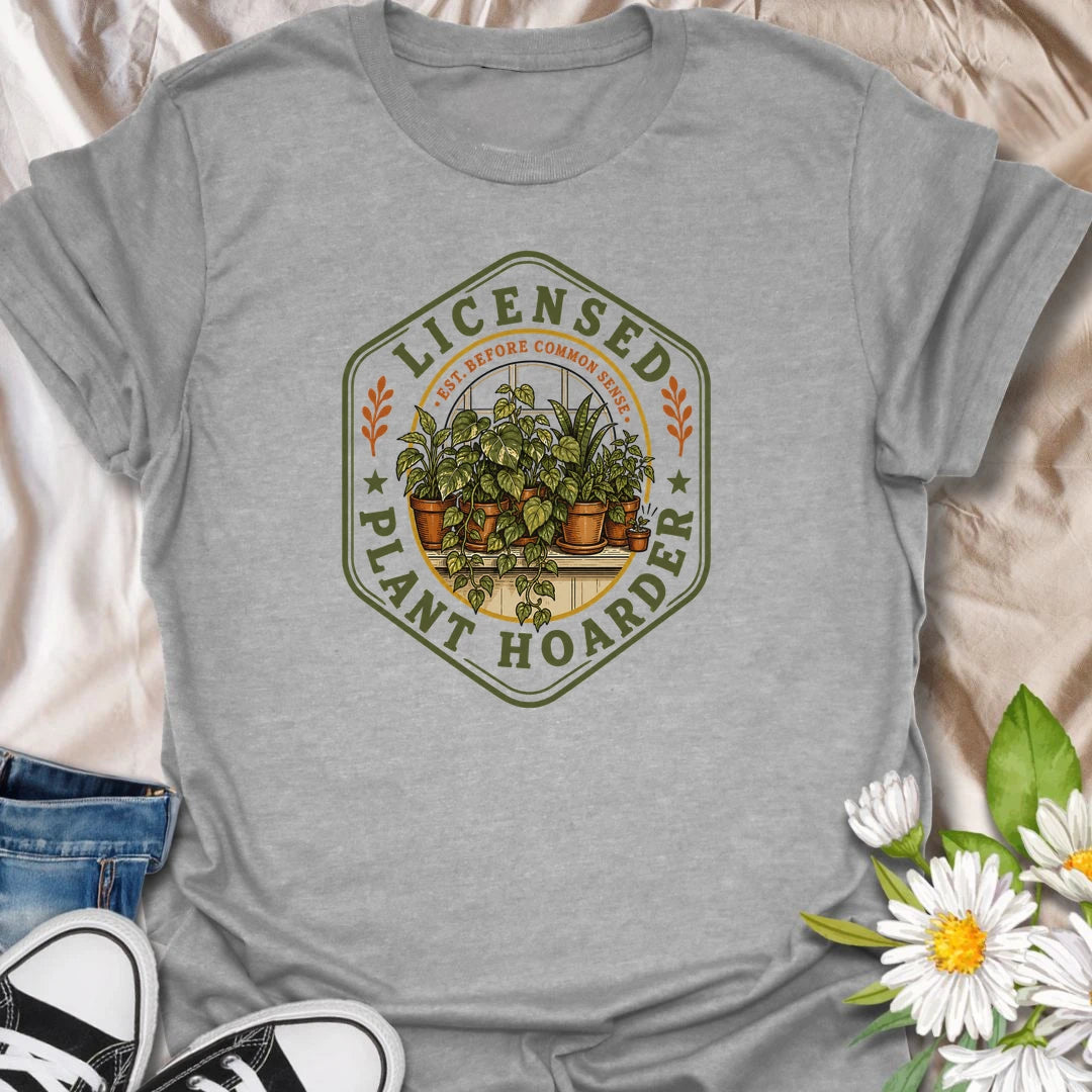 This Licensed Plant Hoarder t-shirt is made for houseplant lovers who ran out of space long before they ran out of excuses. Featuring a vintage badge-style design with an overcrowded windowsill full of potted plants, trailing vines, and the phrase Est. Before Common Sense, this tee has a funny plant-collector feel with classic botanical charm. Perfect for plant moms, plant dads, indoor gardeners, houseplant collectors, propagation fans, and anyone proudly licensed to bring home just one more plant.