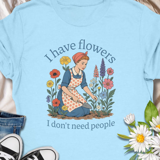 Express your introverted, plant-loving side with this charming floral t-shirt. Perfect for gardeners, plant moms, or anyone who finds peace in flowers over people — it's a blooming statement of self-care.  This tee pairs vintage garden charm with a wry sense of independence. A retro-style gardener tends bright, cottage blooms while the caption reads “I have flowers / I don’t need people.” 