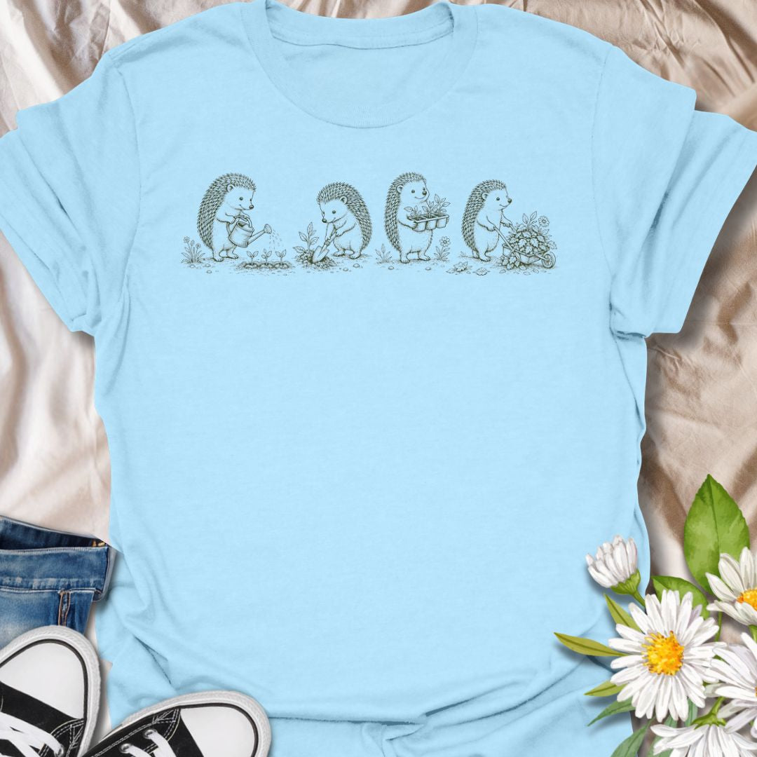 This Gardening Hedgehogs t-shirt is made for gardeners, nature lovers, and woodland animal fans who enjoy sweet vintage-style artwork. Featuring four charming hedgehogs watering, digging, carrying plants, and pushing a flower-filled wheelbarrow, this design has a gentle cottagecore garden feel. Perfect for plant lovers, gardeners, hedgehog fans, wildlife lovers, botanical art fans, and anyone who loves soft nature-inspired designs.