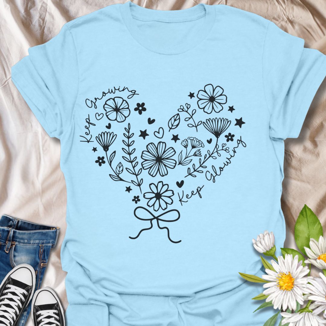 Charming floral heart t-shirt featuring delicate hand-drawn flowers with positive affirmations “Keep Growing, Keep Glowing.” A perfect uplifting gift for gardeners and plant lovers. Light blue