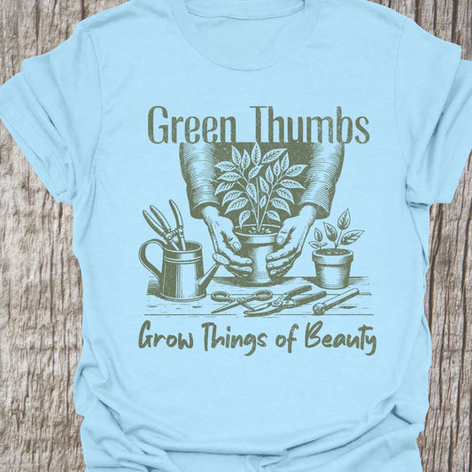 Green Thumbs Grow Things of Beauty text with image of hands holding a plant pot and garden implements around on a light blue t-shirt