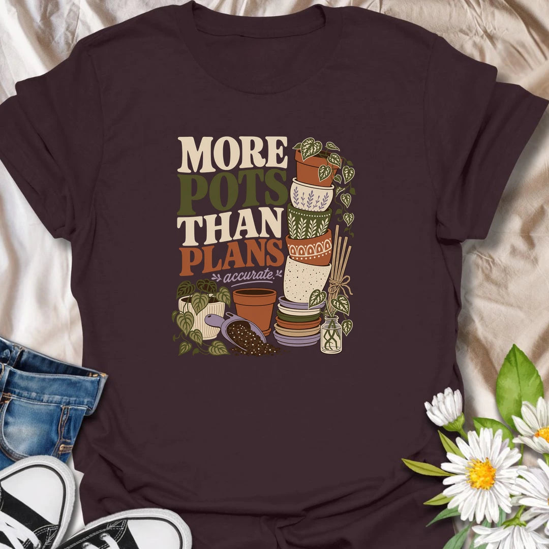 A relatable plant lover T-shirt for anyone whose pot collection has grown faster than their planting plans. The design features a tall stack of decorative pots, trailing houseplants, propagation cuttings, and potting soil. A fun gift for gardeners, plant collectors, and anyone who can never resist another beautiful planter.