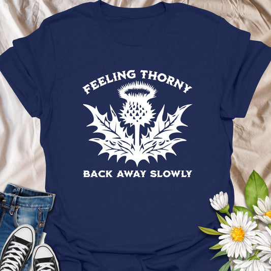 Embrace your mood with this witty “Feeling Thorny – Back Away Slowly” t-shirt featuring a bold thistle graphic. Perfect for introverts, plant lovers, and anyone with a sharp sense of humor, this quirky design makes a great gift or statement piece for everyday wear.