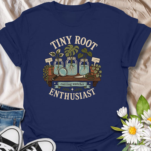 A playful propagation T-shirt for anyone fascinated by the first tiny roots appearing on a cutting. The design features glass jars, water-propagated plants, a magnifying glass, pruning shears, and trailing greenery. A thoughtful gift for houseplant lovers, propagation fans, and patient indoor gardeners.