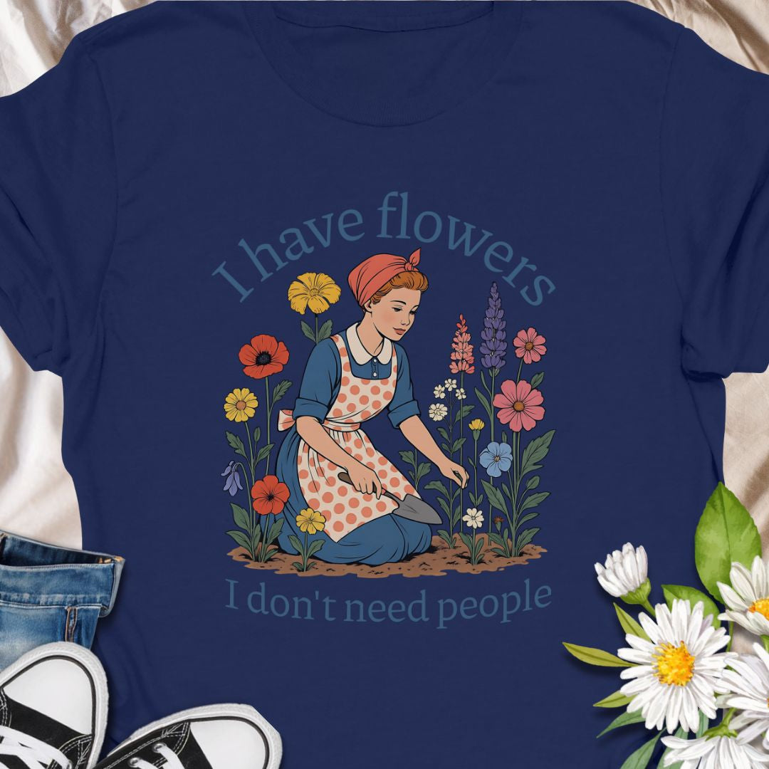 Express your introverted, plant-loving side with this charming floral t-shirt. Perfect for gardeners, plant moms, or anyone who finds peace in flowers over people — it's a blooming statement of self-care.  This tee pairs vintage garden charm with a wry sense of independence. A retro-style gardener tends bright, cottage blooms while the caption reads “I have flowers / I don’t need people.” 