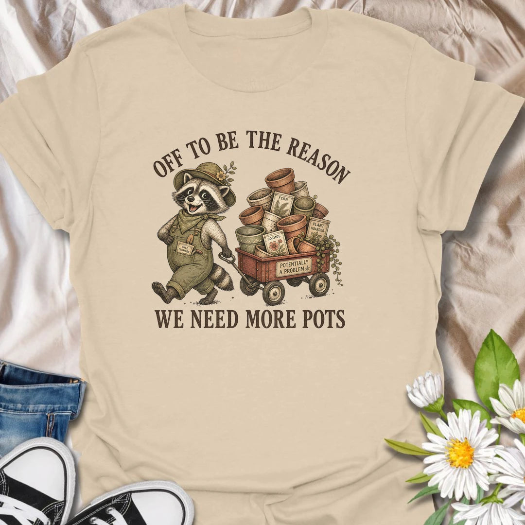 This Off To Be The Reason We Need More Pots t-shirt is perfect for gardeners and plant lovers who always have another plant, cutting, or seedling waiting for a home. Featuring a cheerful raccoon with a wagon full of flower pots, seed packets, and garden supplies, this funny botanical design is great for plant moms, houseplant collectors, gardeners, and anyone who can never have too many pots.