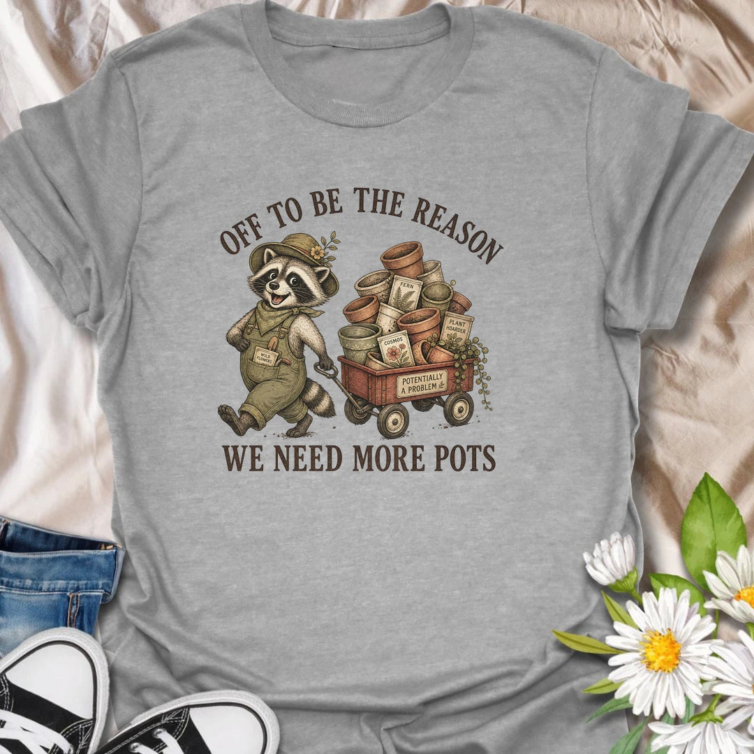 This Off To Be The Reason We Need More Pots t-shirt is perfect for gardeners and plant lovers who always have another plant, cutting, or seedling waiting for a home. Featuring a cheerful raccoon with a wagon full of flower pots, seed packets, and garden supplies, this funny botanical design is great for plant moms, houseplant collectors, gardeners, and anyone who can never have too many pots.