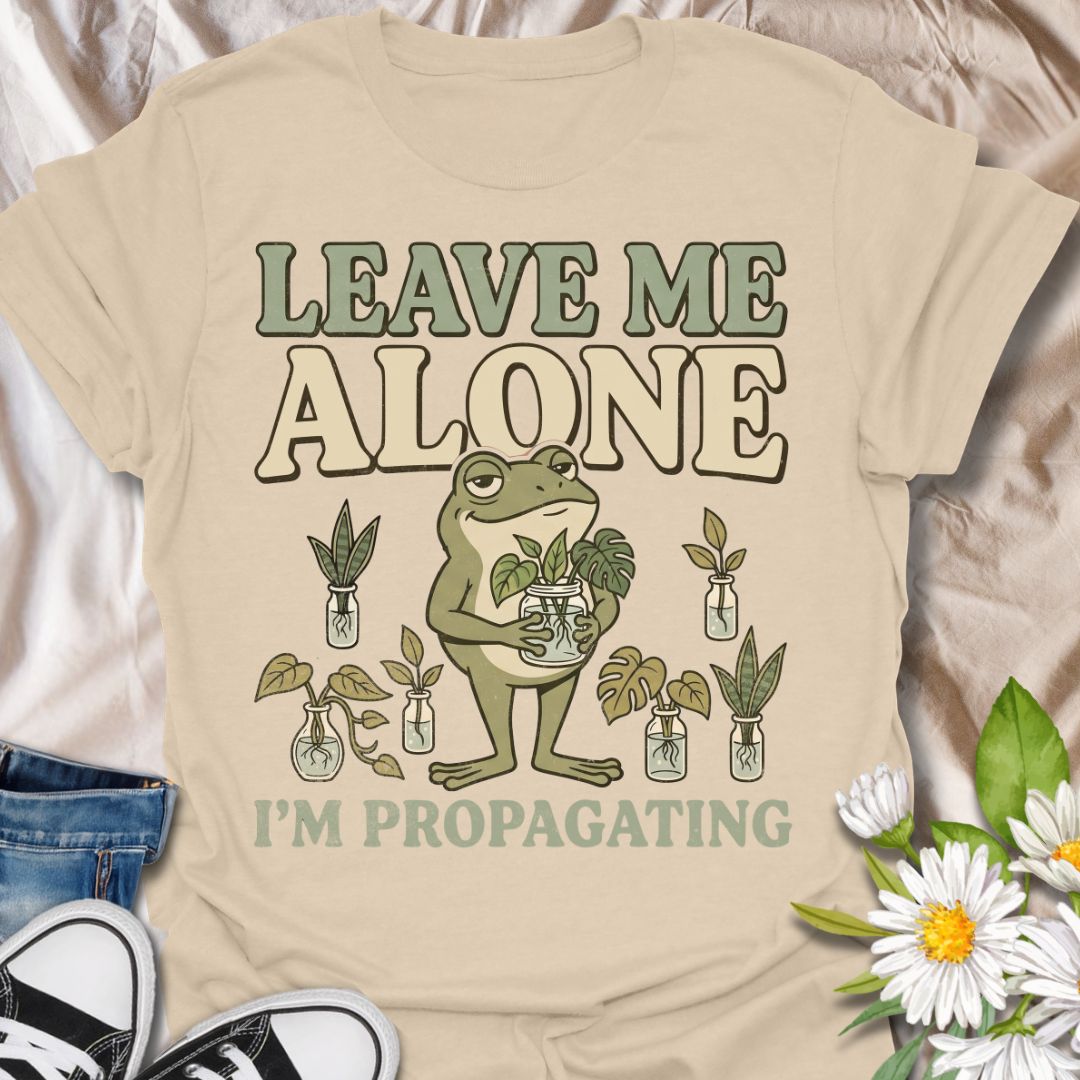 This Leave Me Alone I’m Propagating t-shirt is made for plant lovers who take cuttings, jars, roots, and quiet plant time very seriously. Featuring a smug cartoon frog holding propagated plant cuttings, surrounded by propagation jars, leafy plants, and bold retro lettering, this design has a funny botanical vibe with plenty of plant-parent attitude. Perfect for houseplant lovers, plant moms, propagation fans, indoor gardeners, frog lovers, and anyone who would rather be rooting cuttings than talking to peop