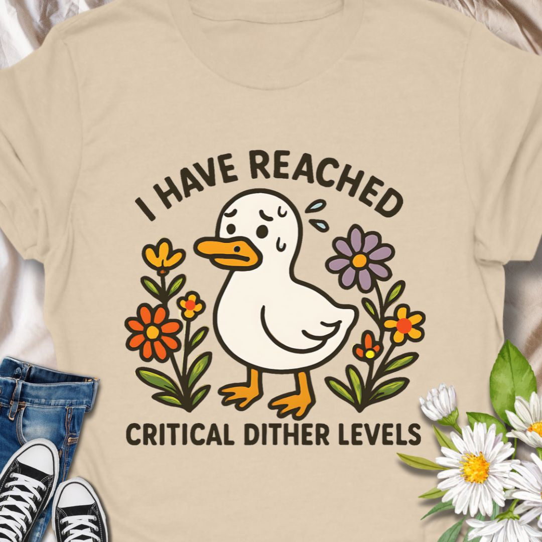 Soft, light, and quietly silly — this tee carries a tiny moment of honest feeling. A cheerful duck illustration stands among simple hand-drawn flowers with the line “I have reached critical dither levels.” Wear it when your brain is doing cartwheels and you need an outfit that says, with humor and a little compassion, “I’m wobbling but still okay.”