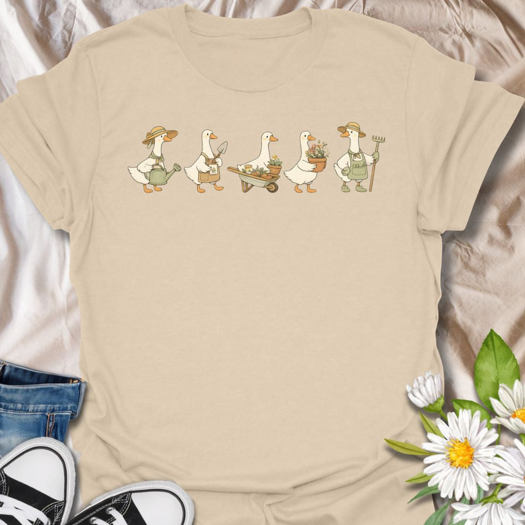 This Gardening Geese t-shirt is made for gardeners, plant lovers, and anyone who enjoys cute nature-inspired artwork with a little humor. Featuring a row of charming geese carrying watering cans, garden tools, flower pots, a wheelbarrow, and fresh plants, this design has a playful cottagecore garden feel that is easy to wear. Perfect for gardeners, duck lovers, plant moms, flower fans, backyard growers, and anyone who thinks garden chores are better with a gaggle of helpful Geese.