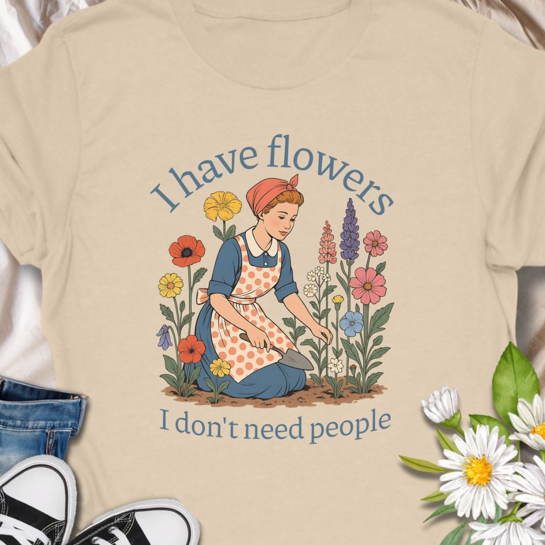 Express your introverted, plant-loving side with this charming floral t-shirt. Perfect for gardeners, plant moms, or anyone who finds peace in flowers over people — it's a blooming statement of self-care.  This tee pairs vintage garden charm with a wry sense of independence. A retro-style gardener tends bright, cottage blooms while the caption reads “I have flowers / I don’t need people.” 