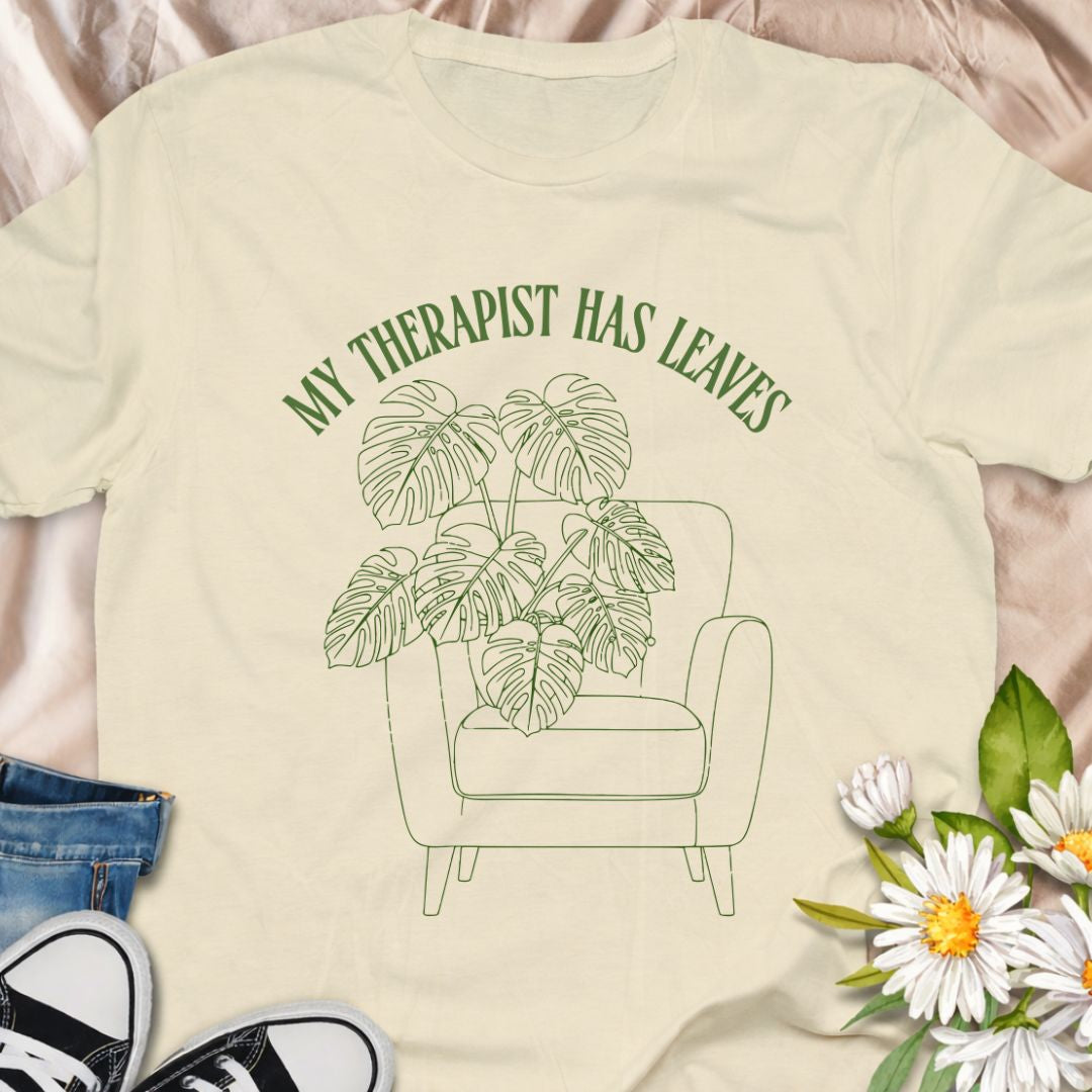 For plant people who spill their heart out to their houseplants, this “My Therapist Has Leaves” t-shirt says it all. Features a cozy armchair and lush monstera, making it the perfect aesthetic plant lover tee for self-care days.