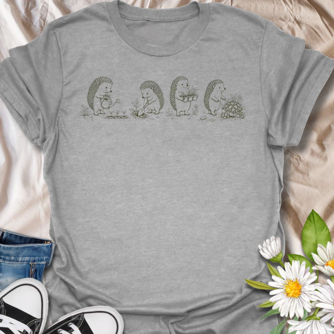 This Gardening Hedgehogs t-shirt is made for gardeners, nature lovers, and woodland animal fans who enjoy sweet vintage-style artwork. Featuring four charming hedgehogs watering, digging, carrying plants, and pushing a flower-filled wheelbarrow, this design has a gentle cottagecore garden feel. Perfect for plant lovers, gardeners, hedgehog fans, wildlife lovers, botanical art fans, and anyone who loves soft nature-inspired designs.