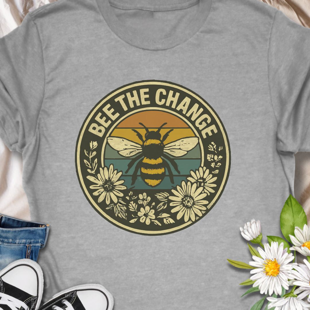 Spread positivity and environmental awareness with this vintage-style “Bee The Change” t-shirt. Featuring a bold bee illustration surrounded by wildflowers and retro sunset colors, it’s perfect for nature lovers, pollinator protectors, and eco-conscious souls. Makes a thoughtful gift for beekeepers, gardeners, or anyone who believes in making a difference—one bee at a time.