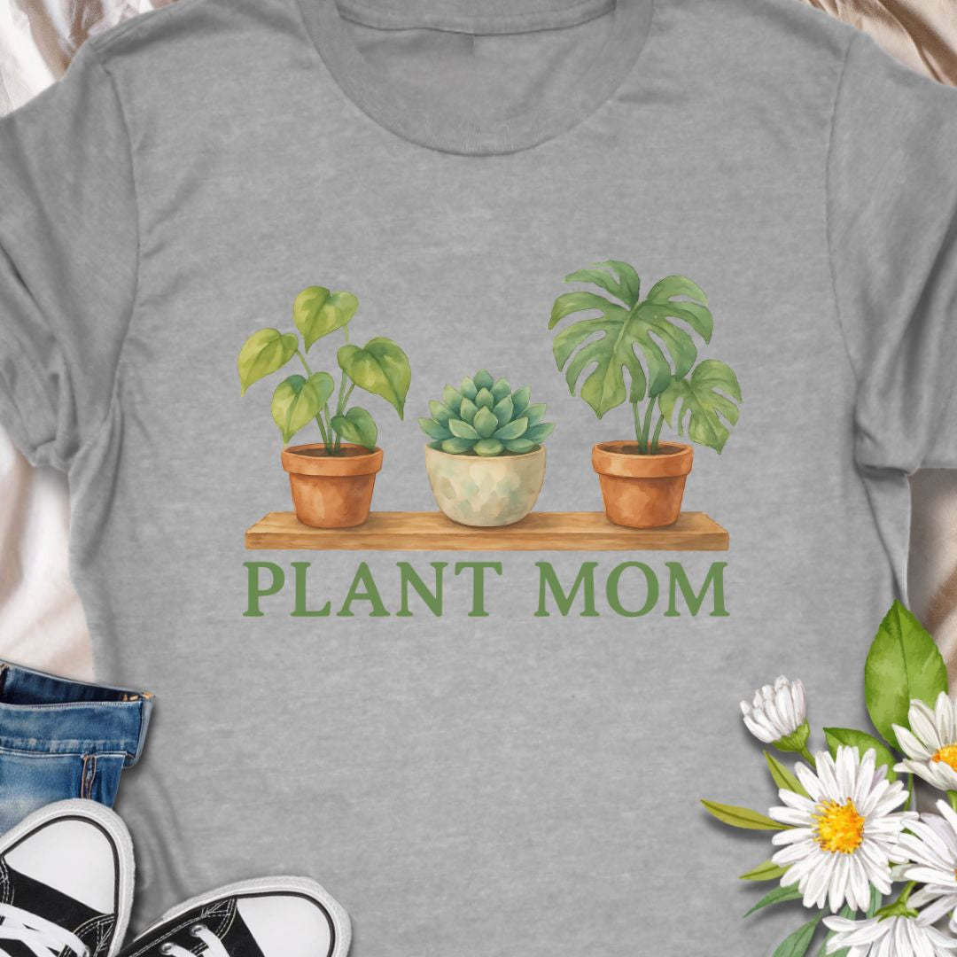 Show off your green thumb with this charming “Plant Mom” t-shirt featuring potted plants on a wooden shelf. Ideal for plant lovers, indoor gardeners, or anyone who adores succulents and tropical houseplants. This tee makes a perfect gift for Mother's Day, birthdays, or just to treat yourself with botanical flair.