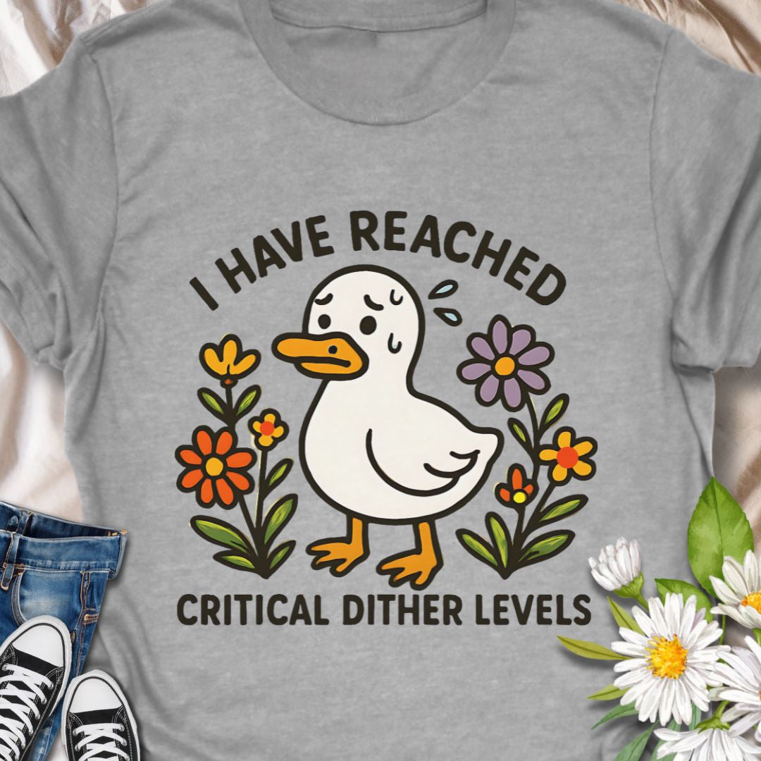 Soft, light, and quietly silly — this tee carries a tiny moment of honest feeling. A cheerful duck illustration stands among simple hand-drawn flowers with the line “I have reached critical dither levels.” Wear it when your brain is doing cartwheels and you need an outfit that says, with humor and a little compassion, “I’m wobbling but still okay.”