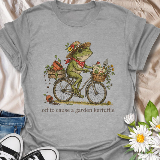 Funny gardening t-shirt featuring a whimsical frog riding a bike with flowers, seeds, and pots, plus the phrase “Off to Cause a Garden Kerfuffle.” Perfect for gardeners, plant lovers, frog fans, and cottagecore garden style lovers.