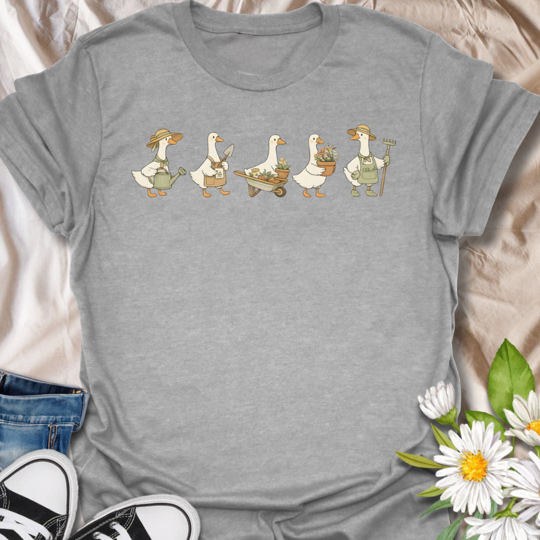 This Gardening Geese t-shirt is made for gardeners, plant lovers, and anyone who enjoys cute nature-inspired artwork with a little humor. Featuring a row of charming geese carrying watering cans, garden tools, flower pots, a wheelbarrow, and fresh plants, this design has a playful cottagecore garden feel that is easy to wear. Perfect for gardeners, duck lovers, plant moms, flower fans, backyard growers, and anyone who thinks garden chores are better with a gaggle of helpful Geese.