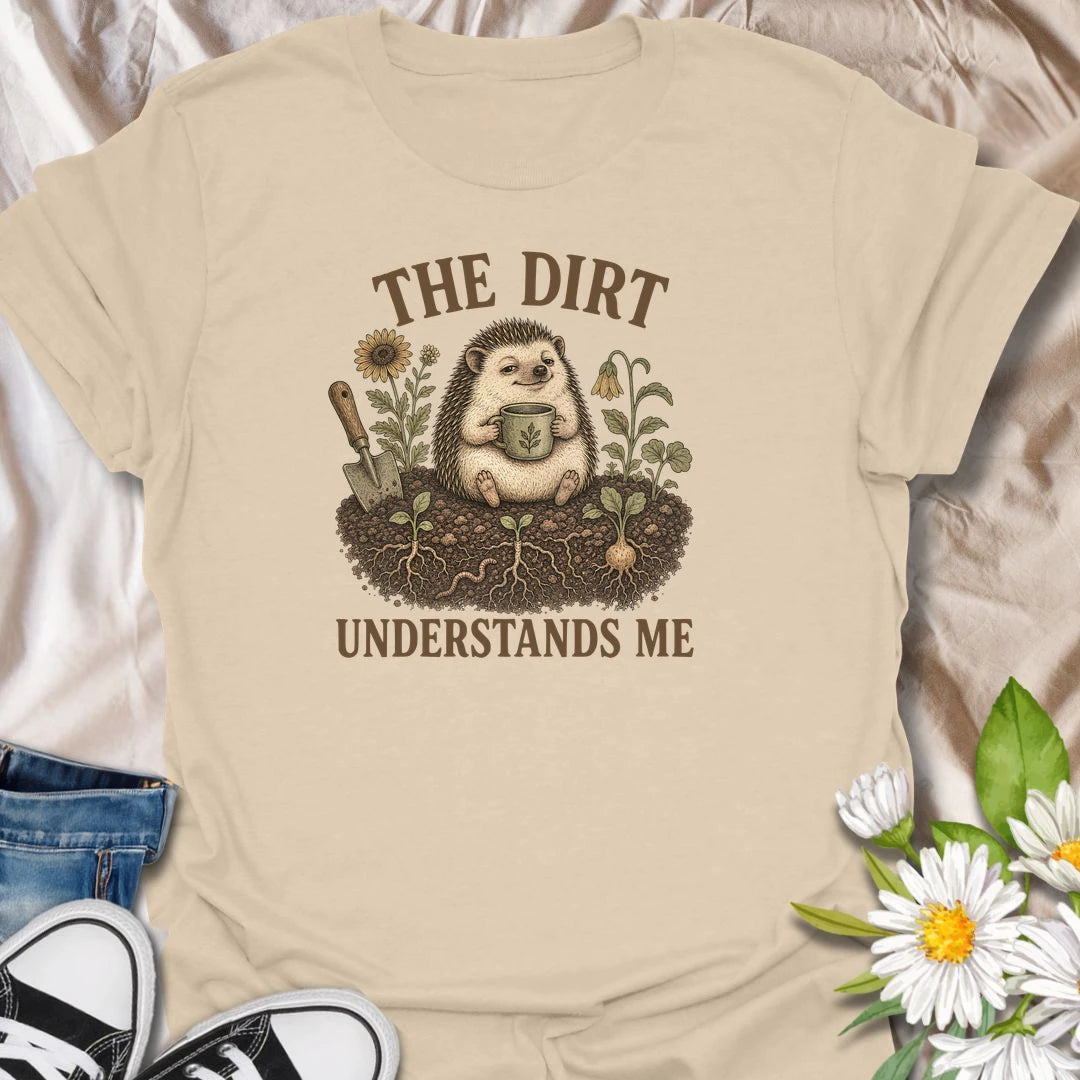 This The Dirt Understands Me t-shirt is perfect for gardeners who feel most at home with soil, seedlings, flowers, and a warm drink nearby. Featuring a cozy hedgehog sitting in the garden with a mug, trowel, roots, blooms, and earthy botanical details, this design is great for plant lovers, backyard gardeners, cottage garden fans, nature lovers, and anyone who feels understood by the dirt.