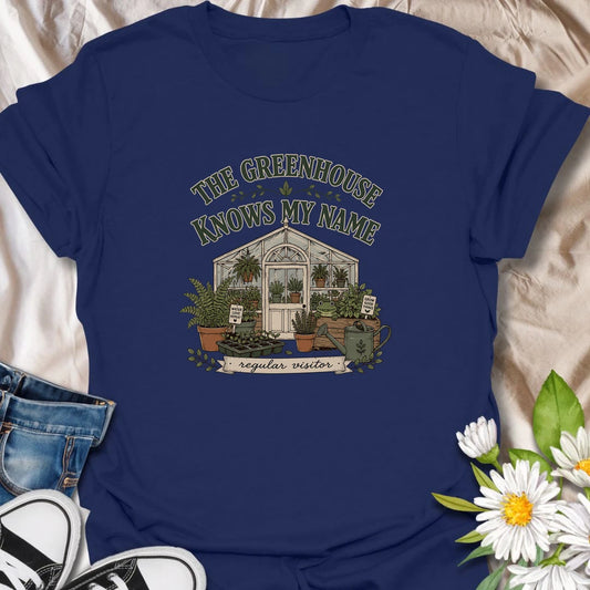 A charming greenhouse T-shirt for gardeners who are regular visitors among the seedlings and potted plants. The design features a traditional greenhouse, ferns, plant trays, a watering can, and a friendly frog. A lovely gift for greenhouse gardeners, plant lovers, and anyone happiest surrounded by growing things.