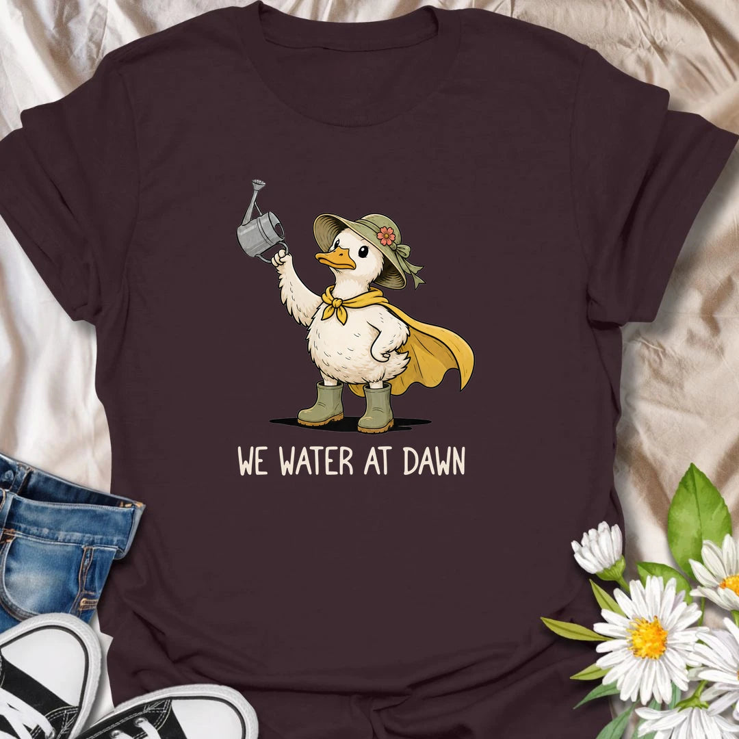 Water At Dawn t-shirt for gardeners who take their morning watering routine very seriously.
The cute duck gardener design adds playful garden charm with boots, a sunhat, cape, and watering can.
It is perfect for plant lovers, cottage garden fans, and anyone who starts the day checking on their flowers.
A sweet and funny gift for gardeners who believe the plants must be watered before anything else happens.