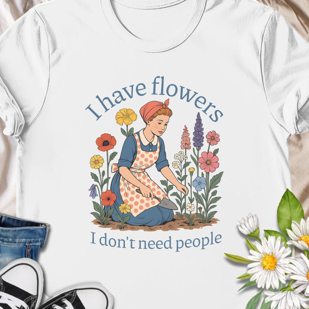 Express your introverted, plant-loving side with this charming floral t-shirt. Perfect for gardeners, plant moms, or anyone who finds peace in flowers over people — it's a blooming statement of self-care.  This tee pairs vintage garden charm with a wry sense of independence. A retro-style gardener tends bright, cottage blooms while the caption reads “I have flowers / I don’t need people.” 