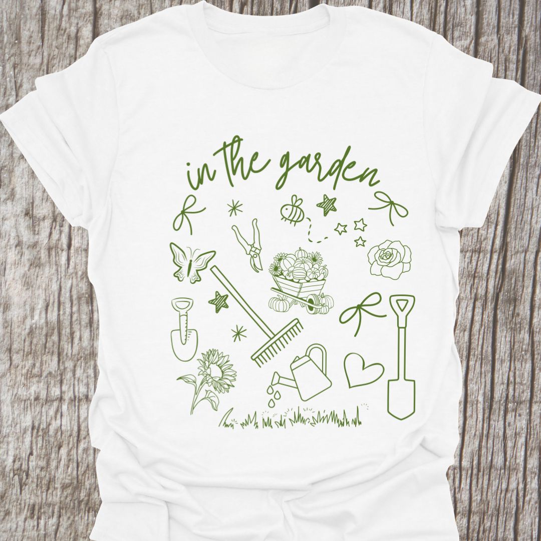 Garden Doodle on a T-shirt!  This doodle has garden tools, flowers, grass, bees, butterfly and lots more, green images and text saying 'in the garden'  on a white t-shirt